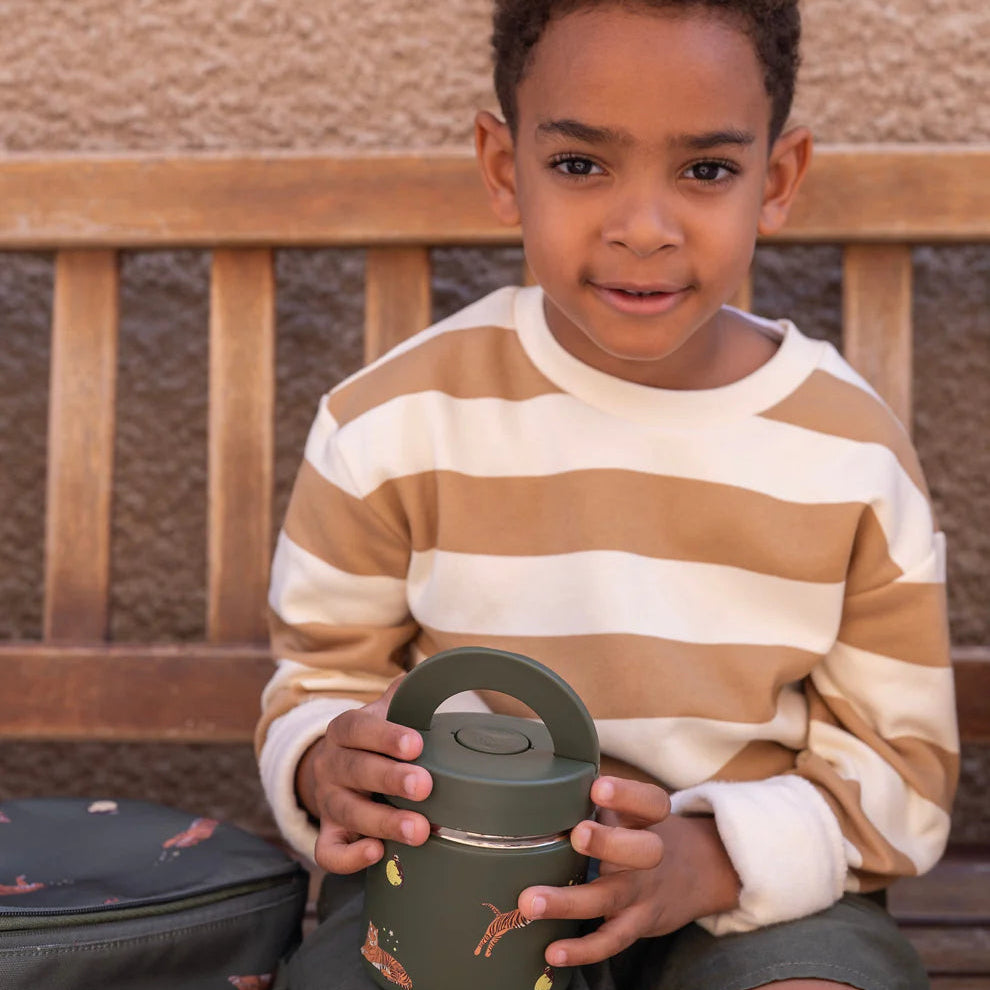 Child holding a green thermos on a wooden bench