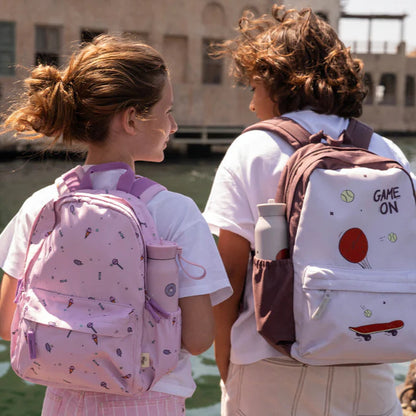 Two people with backpacks standing by a waterfront with buildings in the background
